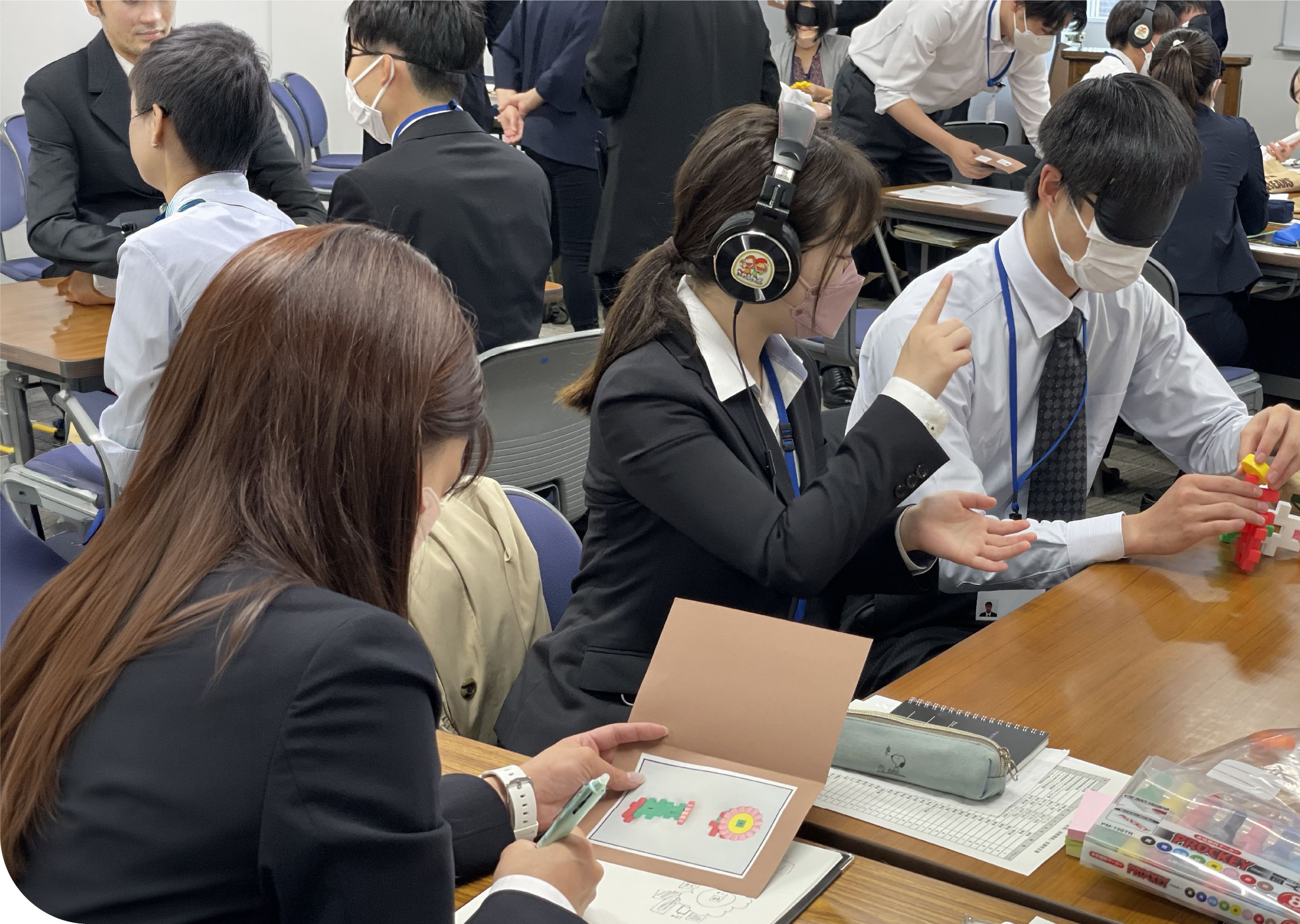 ヘッドホンやアイマスクを着けた受講者がグループでワークに取り組む研修の様子